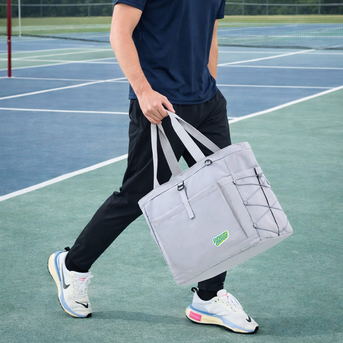 Lightweight Tennis Tote Bag - A grey lightweight tennis tote bag with handles, featuring a logo and elastic bungee cord, carried by a person on a tennis court.