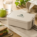 Stack & Go Lunchbox - A beige lunchbox with a logo, placed on a table beside a sandwich, an apple, a glass of water, and a cloth.