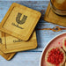 Aroma Coffee Coasters - A set of bamboo coasters featuring a logo, placed on a wooden table alongside a drink and cookies.
