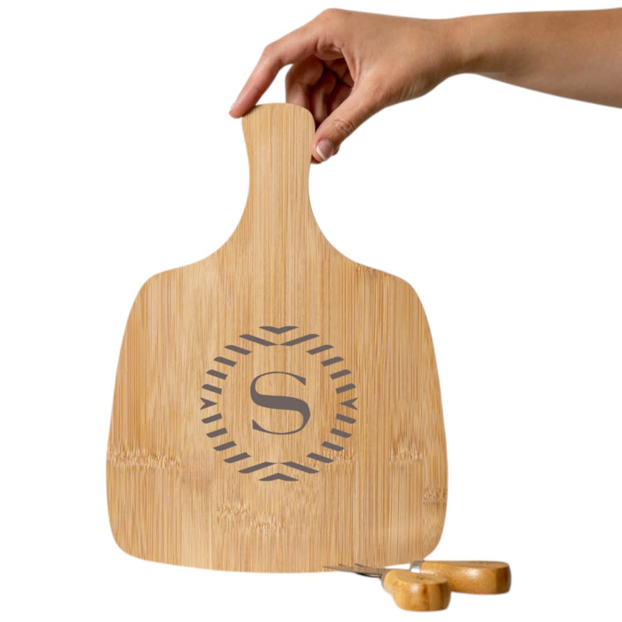 Artis Cheeseboard & Knife Set - A bamboo cheeseboard with an engraved logo and a hand holding it. Two wooden cheese knives are nearby.