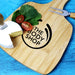 Artis Cheeseboard & Knife Set - A bamboo cheeseboard with a cheese wedge, cherry tomatoes, leafy greens, and a knife. Features a logo.