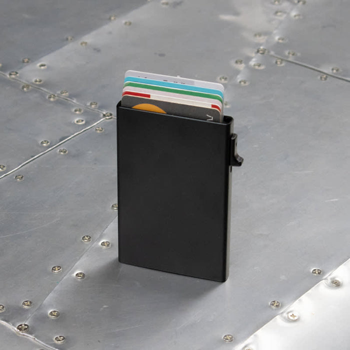 Wally Mag RFID Case - A black RFID case holding multiple cards, set against a metallic surface. The case features a clip on the side.