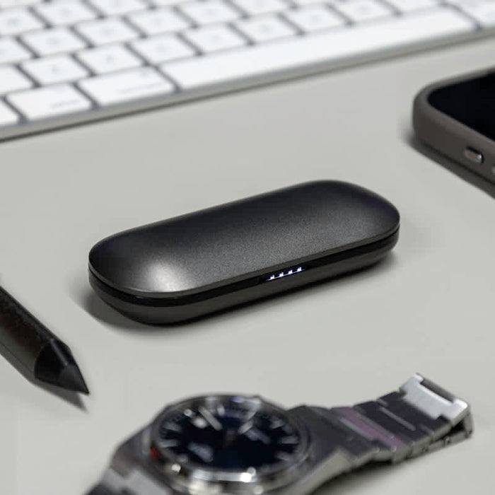 Aria True Wireless Earbuds - A black charging case for true wireless earbuds rests on a desk next to a watch, a smartphone, and a pen.