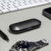Aria True Wireless Earbuds - A black charging case for true wireless earbuds rests on a desk next to a watch, a smartphone, and a pen.