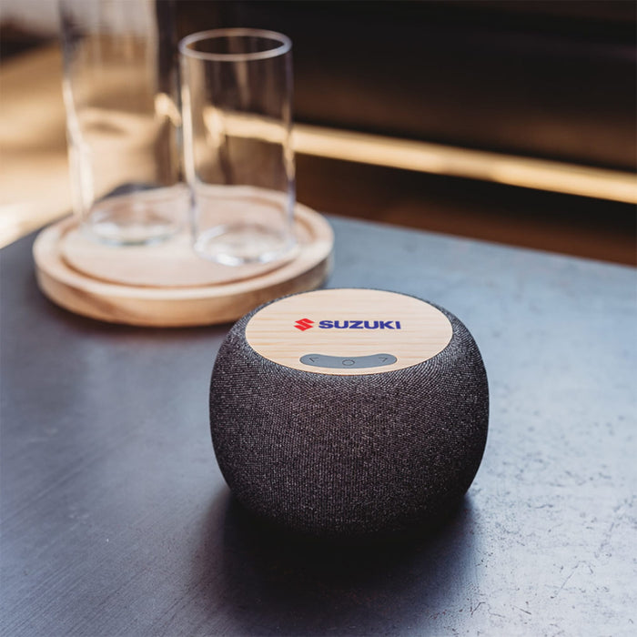 Boomer Bamboo Wireless Speaker - A wireless speaker with a bamboo top and a dark fabric body, featuring a logo on the top.