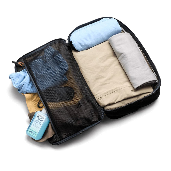 Bellroy Lite Packing Cube 12L - A packing cube in black, filled with rolled clothing items and a bottle of wash liquid. It has a mesh section and a logo.