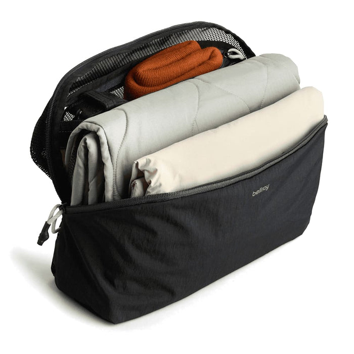 Bellroy Lite Packing Cube 6L - A black packing cube filled with a grey blanket, a beige item, and an orange accessory, featuring a mesh panel on top.