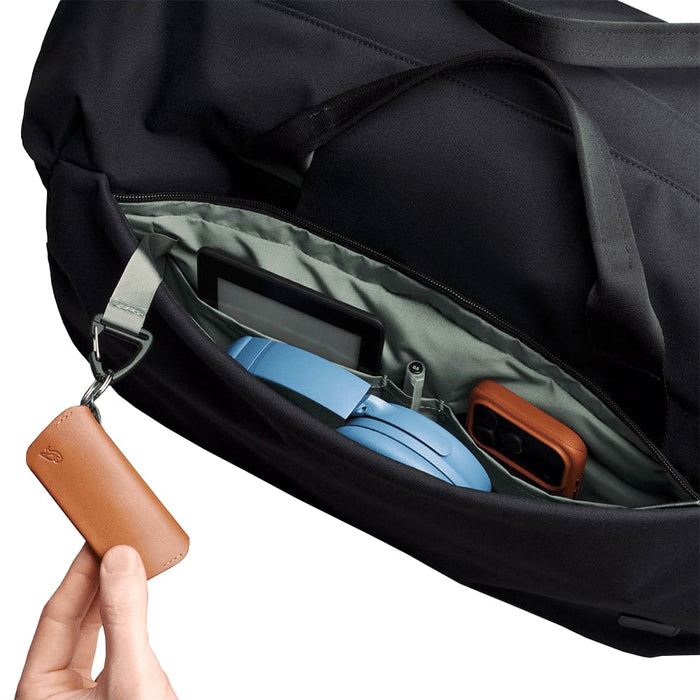 Bellroy Classic Duffel 45L - A close-up of a black duffel bag's interior, featuring a blue headset, a gadget, and a brown leather keychain.