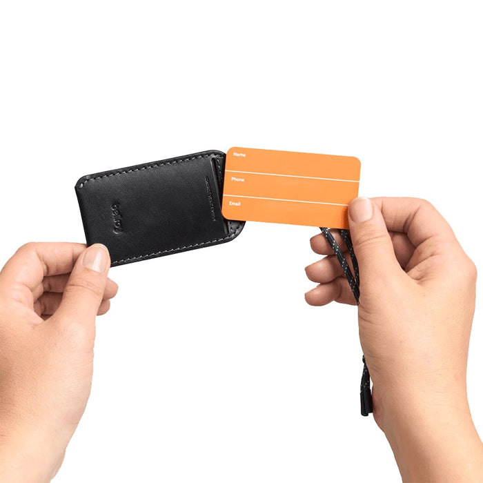 Bellroy Luggage Tag - A black luggage tag is held in hands, revealing an orange identification card with spaces for personal details.