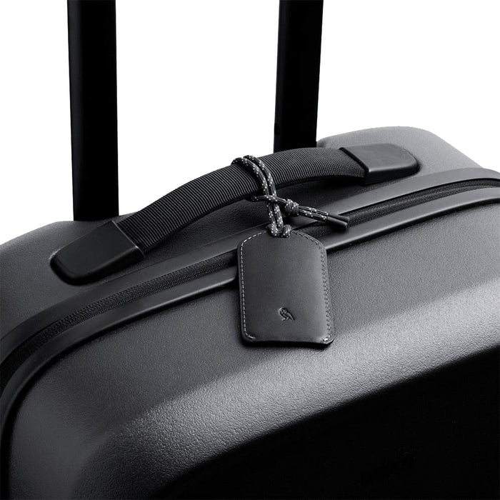 Bellroy Luggage Tag - A black suitcase featuring a sleek leather luggage tag with a braided attachment. It has a minimalist design and a logo.