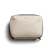 Bellroy Lite Tech Kit - A beige tech kit with a zip closure and a logo on the front, featuring a textured fabric design.