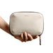 Bellroy Lite Tech Kit - A hand holds a tan Bellroy Lite Tech Kit, featuring a soft-textured exterior and a zip closure.