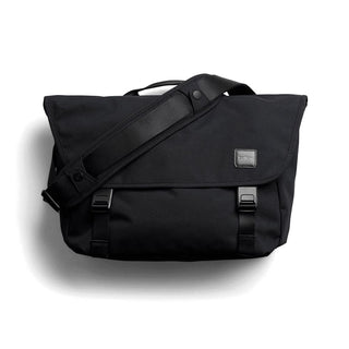 Bellroy Classic Messenger 13L - A black messenger bag with a flap, adjustable shoulder strap, and branding label. It features buckle closures and a sleek design.
