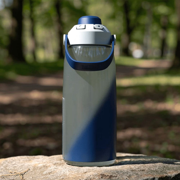CamelBak - Thrive Chug 1.0L - A drink bottle in grey and navy blue, featuring a large handle and a spout, placed on a rock in a natural setting.
