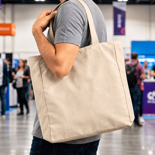 450gsm Victorian Canvas Tote Bag - A person holds a beige 450gsm Victorian canvas tote bag with shoulder straps. The bag features a logo.