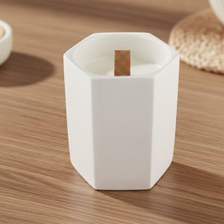 Noosa Hexagon Ceramic Candle - A hexagon-shaped white ceramic candle with a wooden wick, placed on a wooden surface.