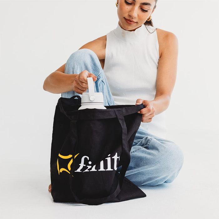 Colourful Calico Tote Bag - A black tote bag with a logo, being held by a person, while they reach inside for a drink bottle.