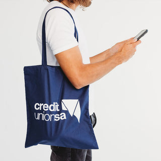 Colourful Calico Tote Bag - A navy blue tote bag with a logo sits over the shoulder of a person holding a smartphone.