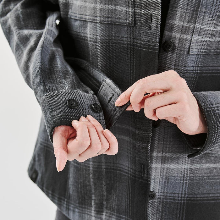 Women's Highland Plaid Shacket - A close-up of a woman's hand adjusting the cuffs of a grey and black plaid shacket featuring buttons.