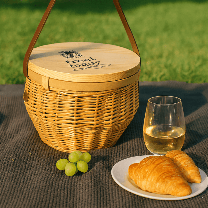 Saint-Rémy Cooler Basket - A wicker cooler basket in natural tones, with a wooden lid, alongside a glass of white wine, grapes, and croissants.