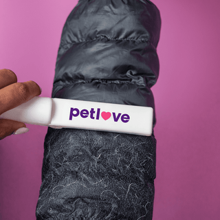 Stick n Roll Lint Remover - A lint remover in white with a logo, removing lint from a black puffer jacket against a pink background.