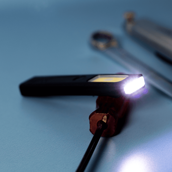 Rechargeable Work Light - A rechargeable work light in black with a bright white LED, placed on a blue surface alongside tools.