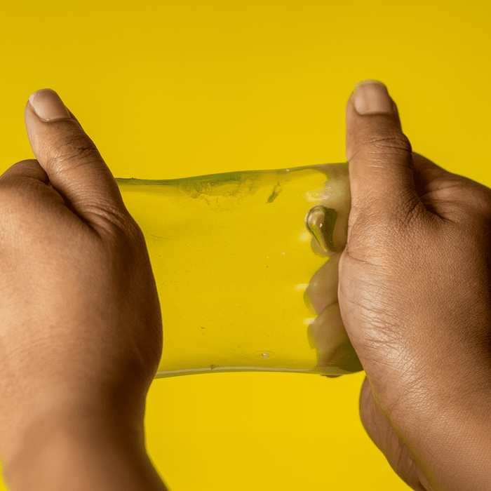 Jelly Cube Sensory Toy - A pair of hands stretching a translucent yellow jelly cube sensory toy against a bright yellow background.