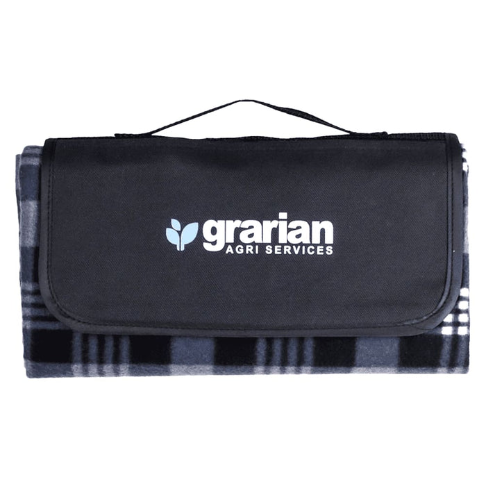 Outdoor Pack - A picnic blanket in grey and black, folded with a carrying handle and a logo on the front.