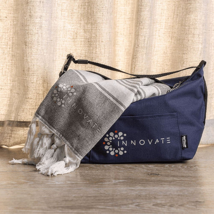 Towel & Cooler Bundle Pack - A navy cooler bag with a grey towel, featuring a logo on both items. The towel has a patterned design.