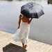 Poppins Umbrella - A black umbrella with a logo, held by a person in a white dress near a water body.