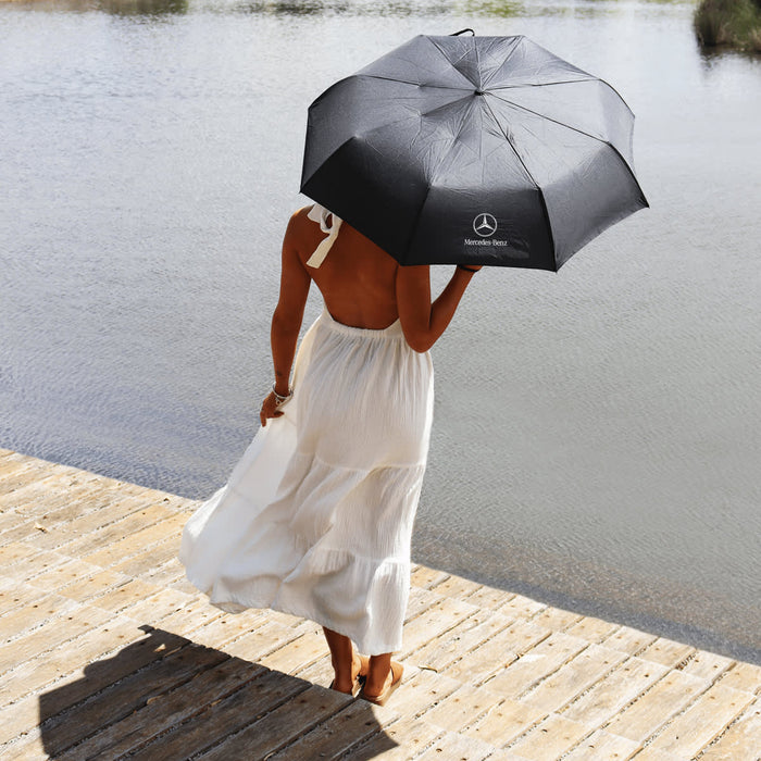 Poppins Umbrella - A black umbrella with a logo held by a person in a white dress, standing by the water.