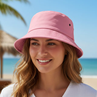 Long Beach Bucket Hat – Medium - A pink bucket hat sits on a smiling woman's head with a beach backdrop and palm trees. The hat features a logo.