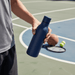 Emily Bottle – 550ml Thermal Drink Bottle - A drink bottle in navy blue held by a person, with sports equipment in the background.