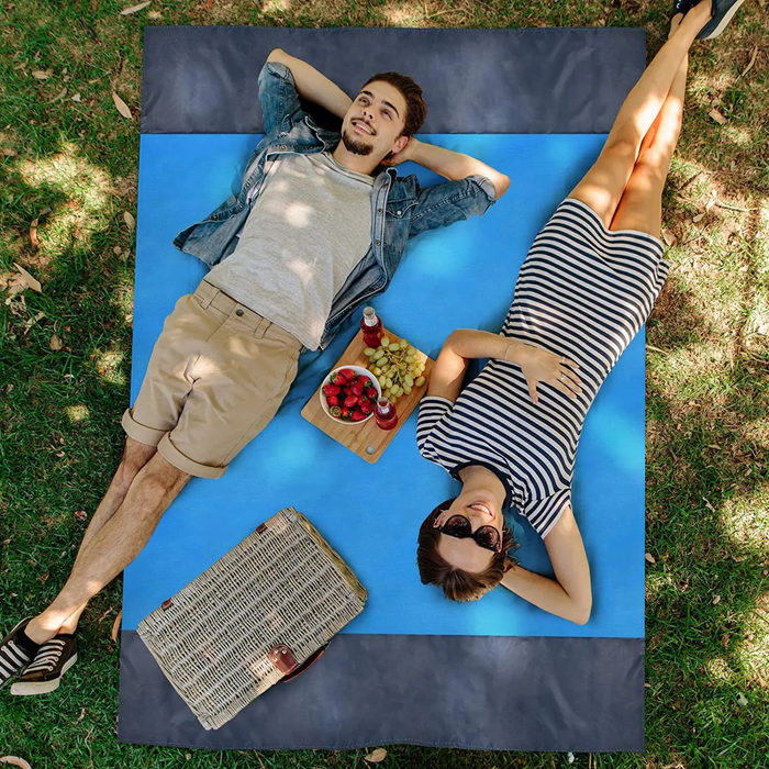 Polyester Picnic Blanket in Pouch - A blue polyester picnic blanket laid out on grass, featuring two people relaxing on it, with picnic items nearby.