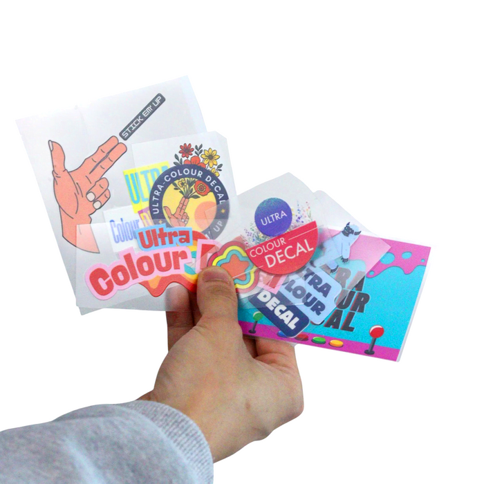 Ultra Colour Decal Sheets - A hand holds several Ultra Colour Decal Sheets featuring various colourful designs and a logo.
