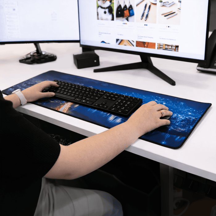 Rubber Desk Mat - A rubber desk mat with a blue cityscape design, placed beneath a keyboard on a workspace.