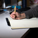 SunScribe Notebook (A4) - A hand holding a pen writes in a cream-coloured lined SunScribe notebook on a desk. The notebook has a blue cover.