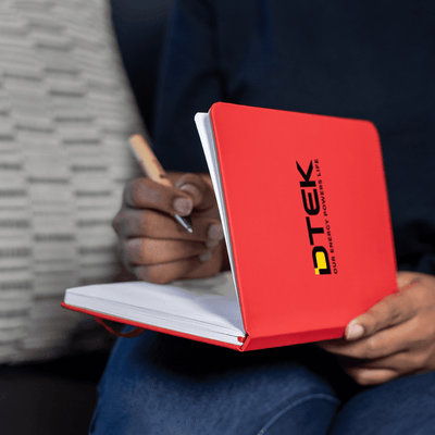 Space A5 Notebook - A red A5 notebook with a logo on the cover, held open with a hand writing inside.