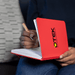 Space A5 Notebook - A red A5 notebook with a logo on the cover, held open with a hand writing inside.