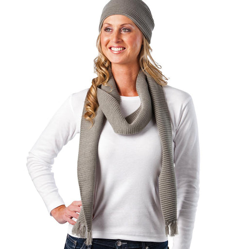 Ruga Knit Scarf - A woman wearing a grey knitted scarf and beanie, with her hair cascading down and a white long-sleeve top.