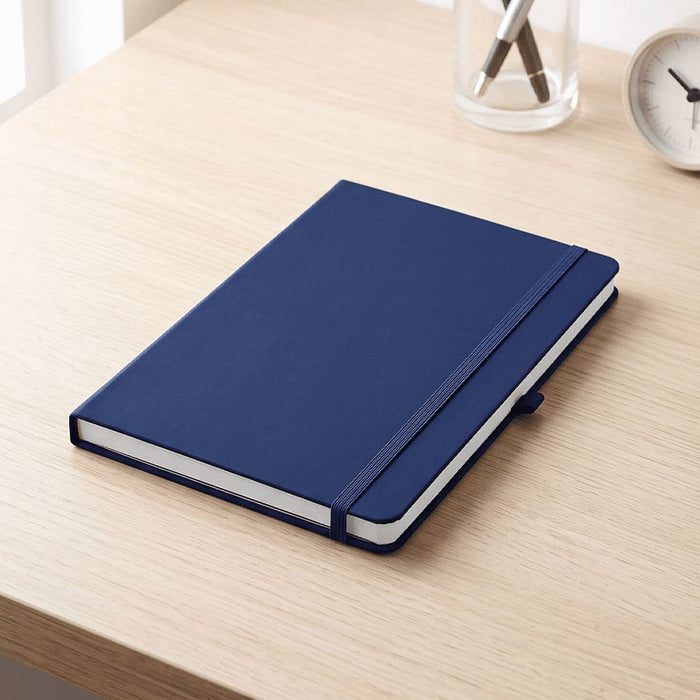 Recycled Spectrum A5 JournalBook - A navy A5 journal with a textured cover, elastic band closure, and white pages, resting on a wooden desk.