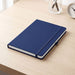 Recycled Spectrum A5 JournalBook - A navy A5 journal with a textured cover, elastic band closure, and white pages, resting on a wooden desk.