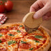 Bamboo Pizza Cutter - A bamboo pizza cutter with a rounded handle cuts through a pepperoni pizza on a wooden surface.