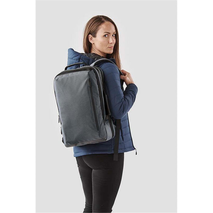 Hedmark Commuter Backpack - A woman wearing a navy jacket carries a grey Hedmark Commuter Backpack, featuring multiple compartments and a logo.