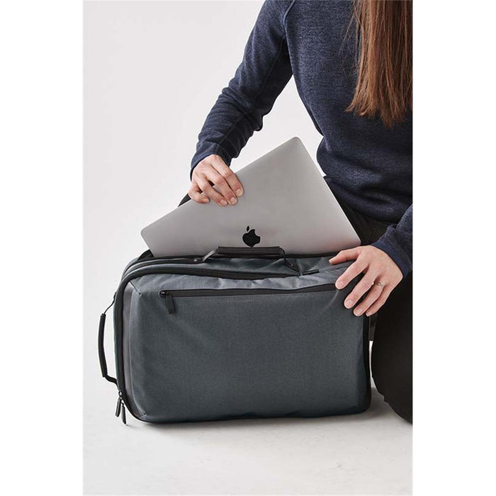 Hedmark Commuter Backpack - A grey laptop backpack with a person placing a silver laptop inside, featuring a front pocket and a logo.