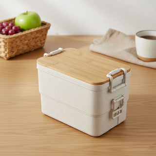 Bamboo Stack & Go Lunch Box - A beige bamboo stackable lunch box with a wooden lid, placed on a wooden surface beside a woven basket and cup.