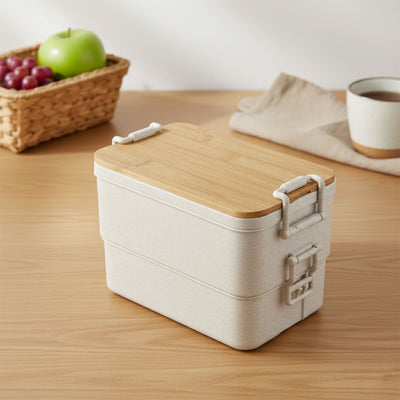 Bamboo Stack & Go Lunch Box - A beige bamboo stackable lunch box with a wooden lid, placed on a wooden surface beside a woven basket and cup.