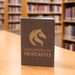 The Barker Eco Notebook - B6 - A brown eco notebook with a logo on the cover, placed on a wooden table in a library setting.