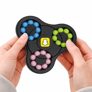 The Spin Buddy Puzzle Game - A hands holding a black puzzle game featuring blue, green, pink, and yellow components with a logo in the centre.