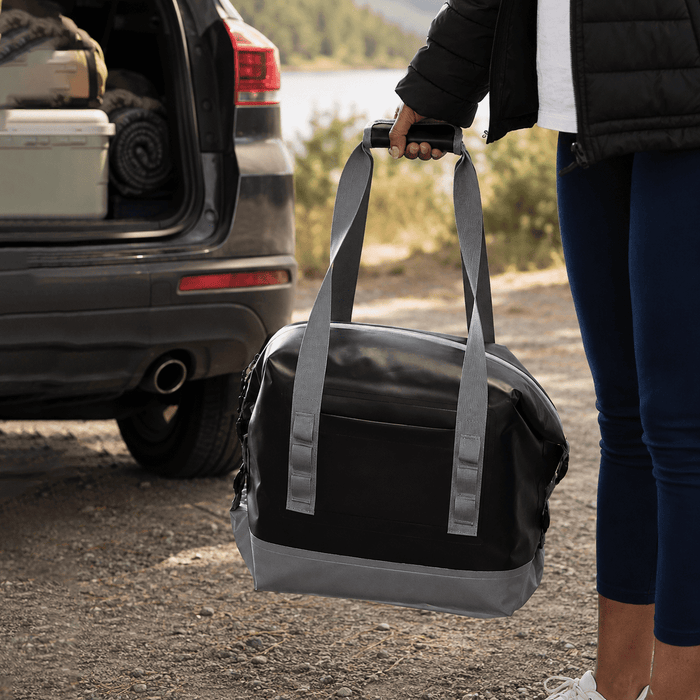 Premium 17L Foldable Cooler - A foldable cooler in black and grey, held by a person near the back of a vehicle. It has carrying straps and a logo.
